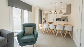 A modern kitchen with a dining area, featuring a teal armchair, white chairs, and pendant lighting.