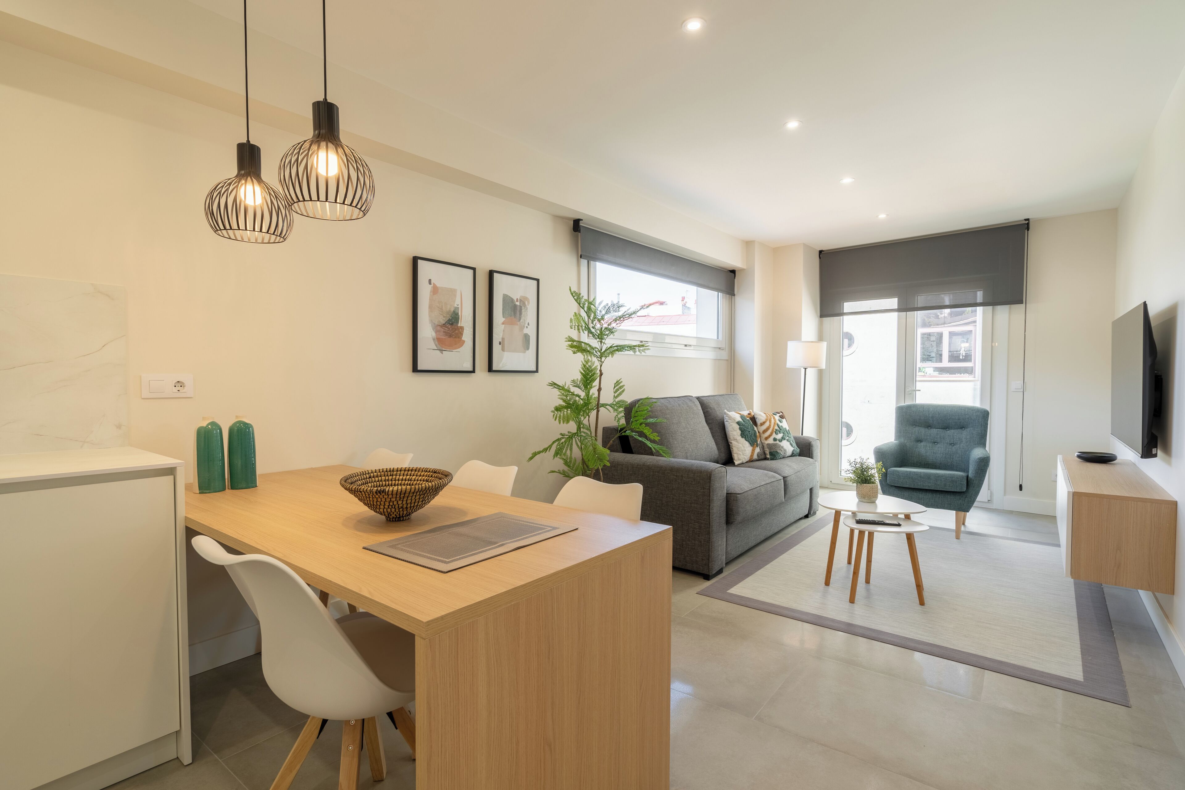 Un salon moderne avec un canapé, un coin repas comprenant une table et des chaises, un téléviseur fixé au mur et une grande fenêtre offrant une vue dégagée.