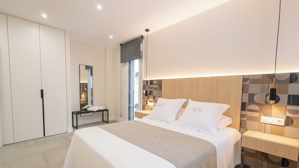 A modern bedroom with a large bed, bedside tables, a mirror, and a wardrobe.
