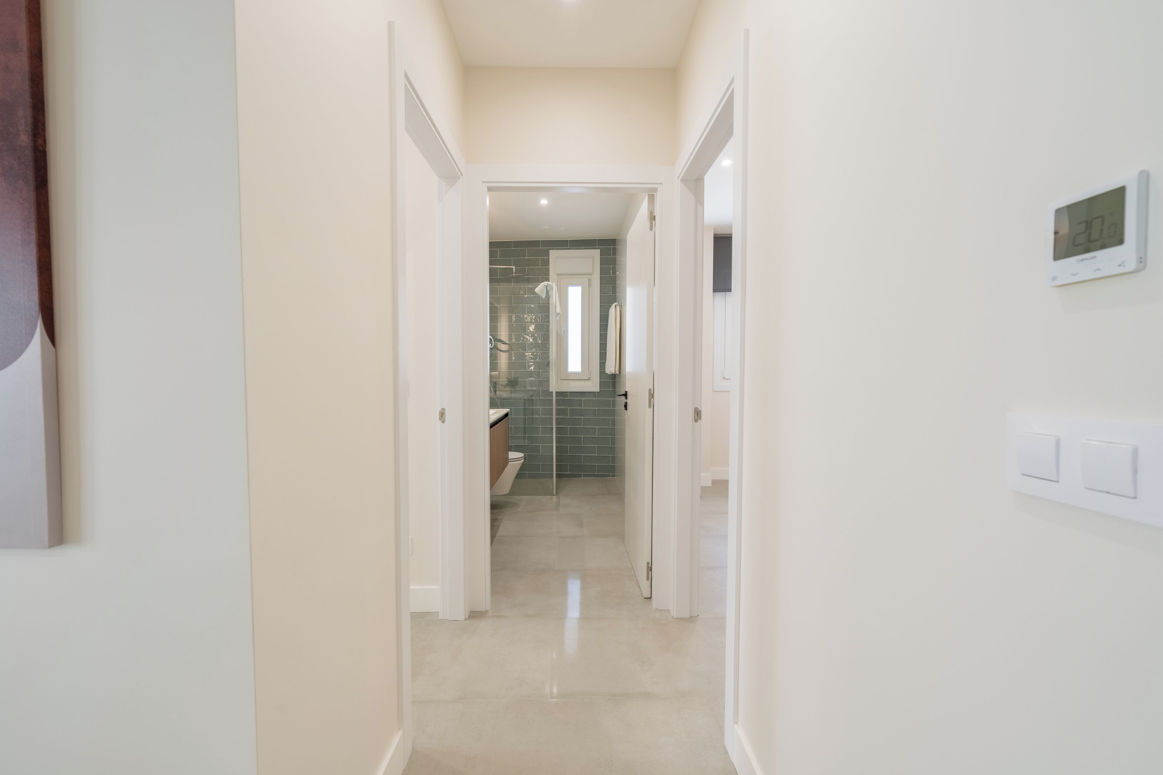 A hallway leading to a bathroom with a toilet, a shower, and a tiled wall.