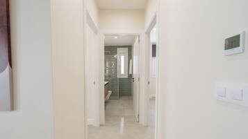 A hallway leading to a bathroom with a toilet, a shower, and a tiled wall.