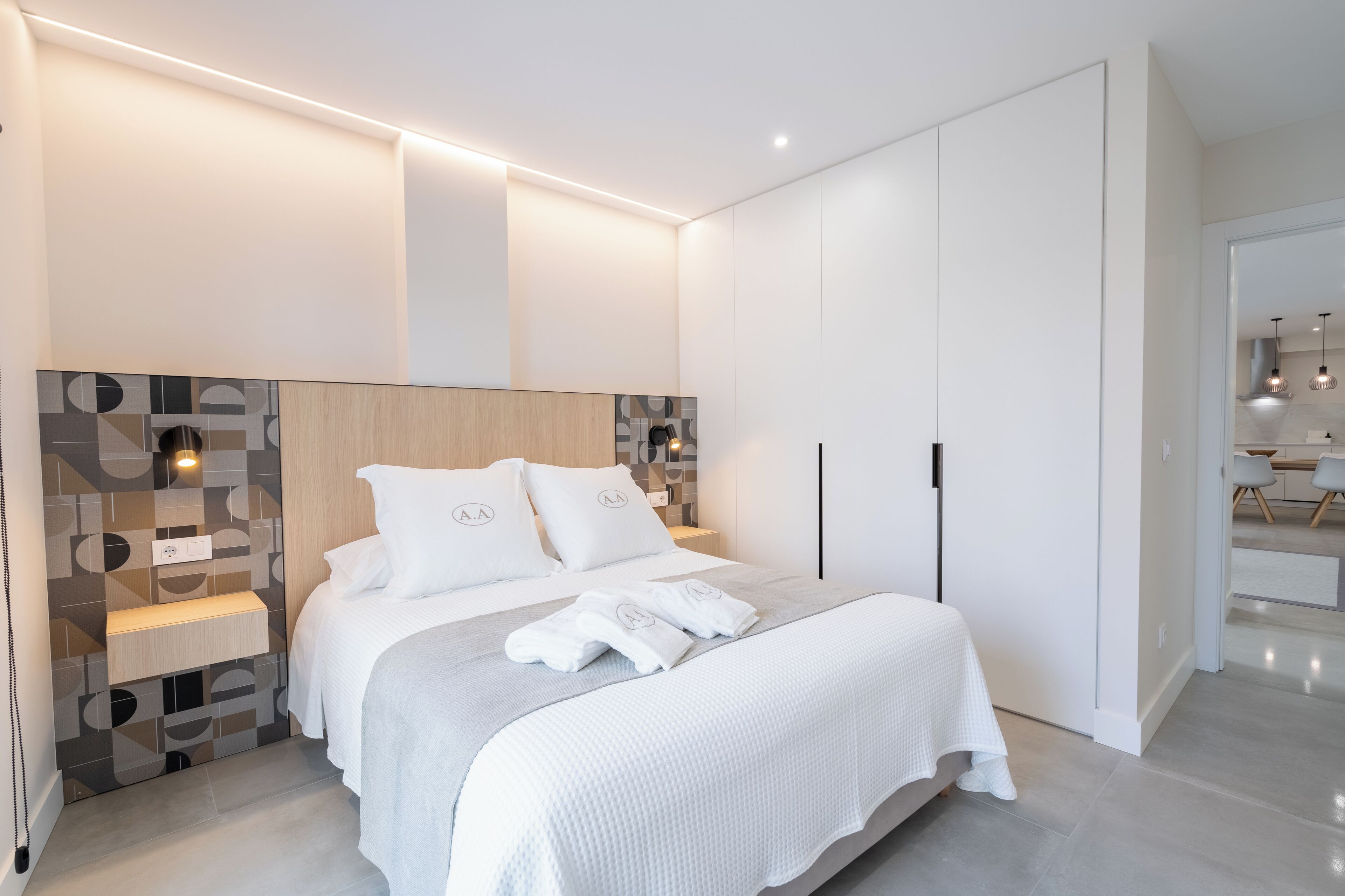 A modern bedroom with a large bed, built-in wardrobe, and a bedside table.