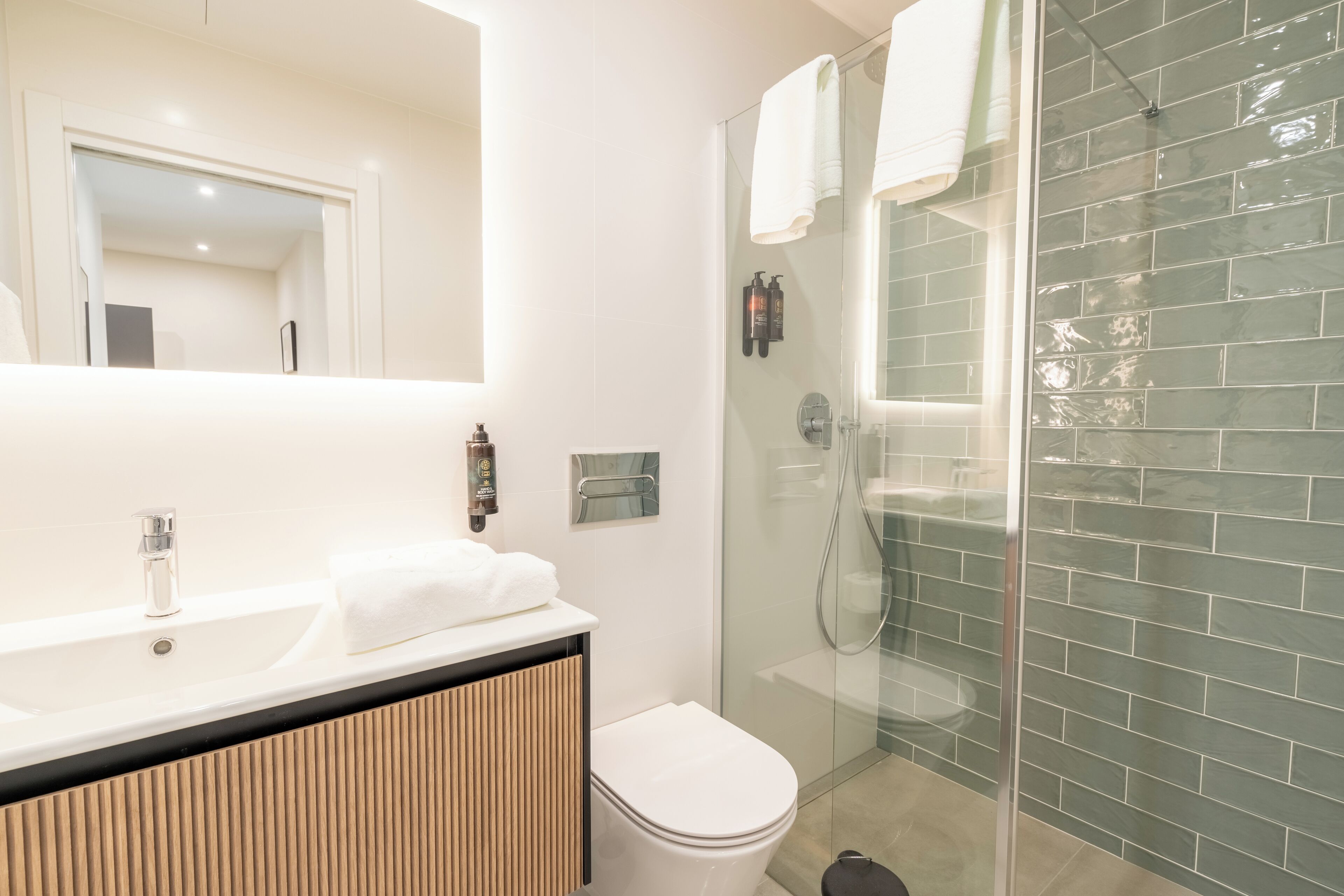 Une salle de bain moderne avec une douche à parois de verre, un lavabo blanc et un meuble-vasque en bois, ainsi que des toilettes.