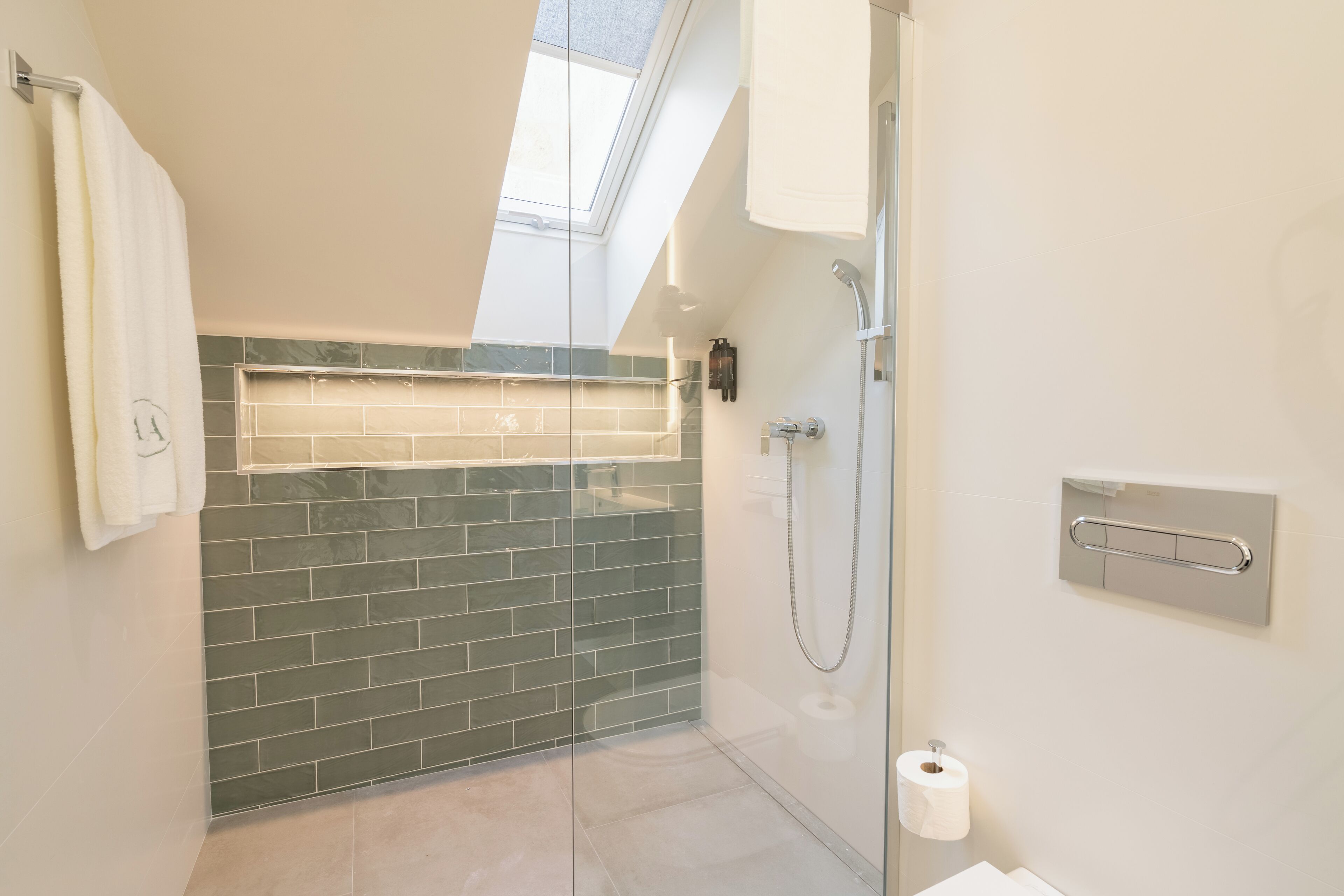 Een moderne badkamer met dakraam, glazen douchecabine en betegelde spatwand.
