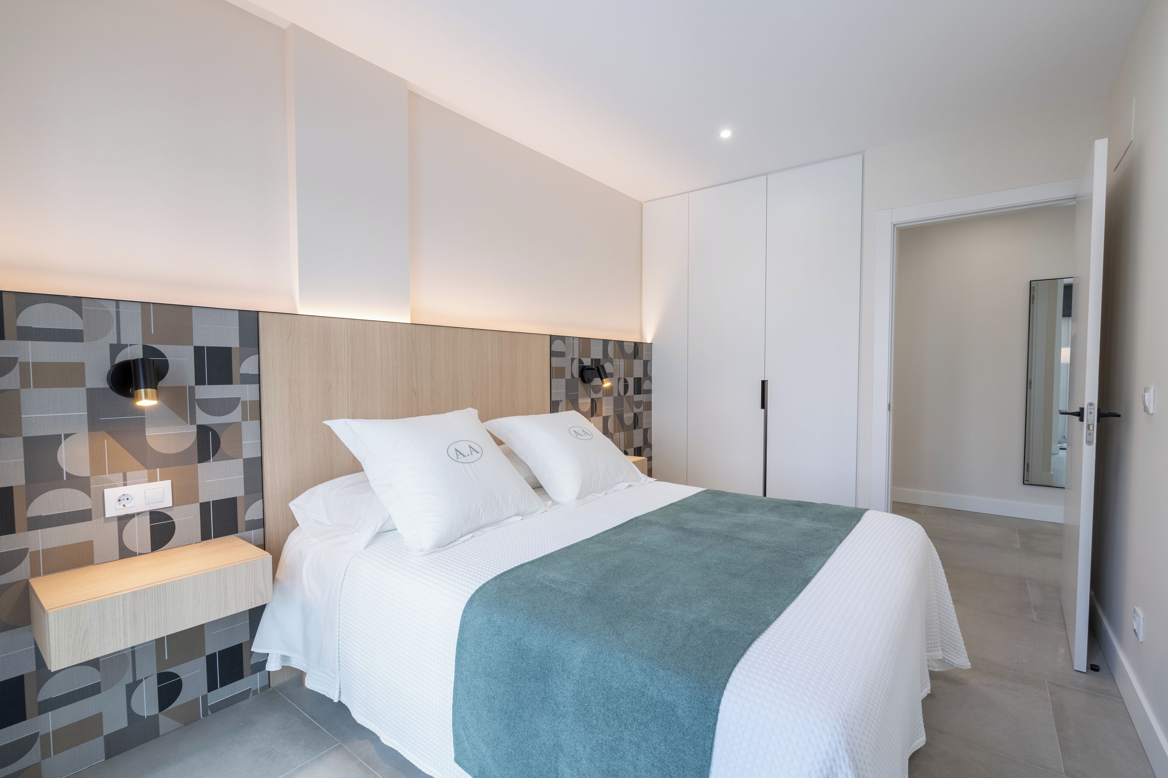 Een moderne slaapkamer met een bed, nachtkastje en een wandlamp.