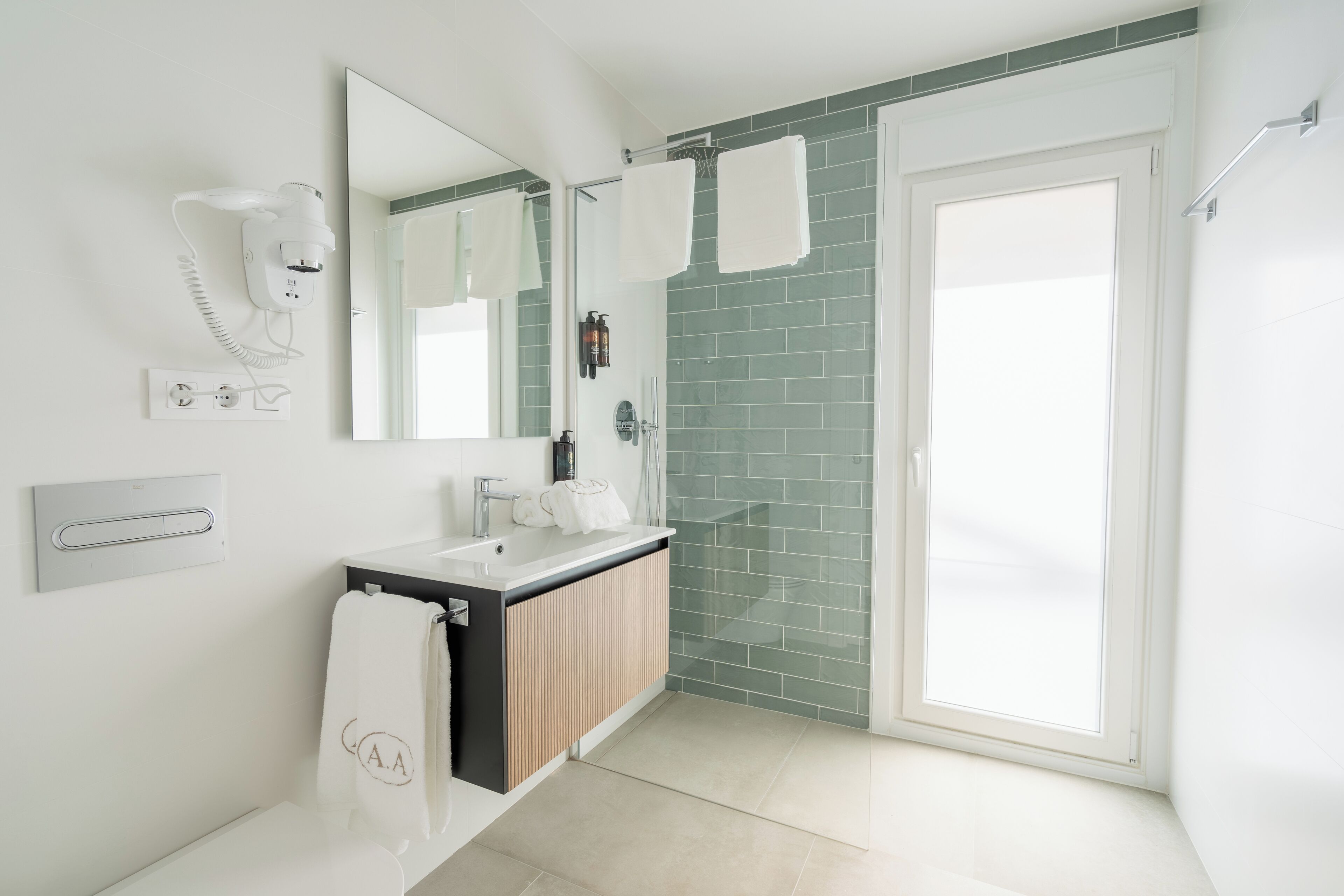 A modern bathroom with a white sink, a mirror, a towel rack, and a green-tiled shower area.