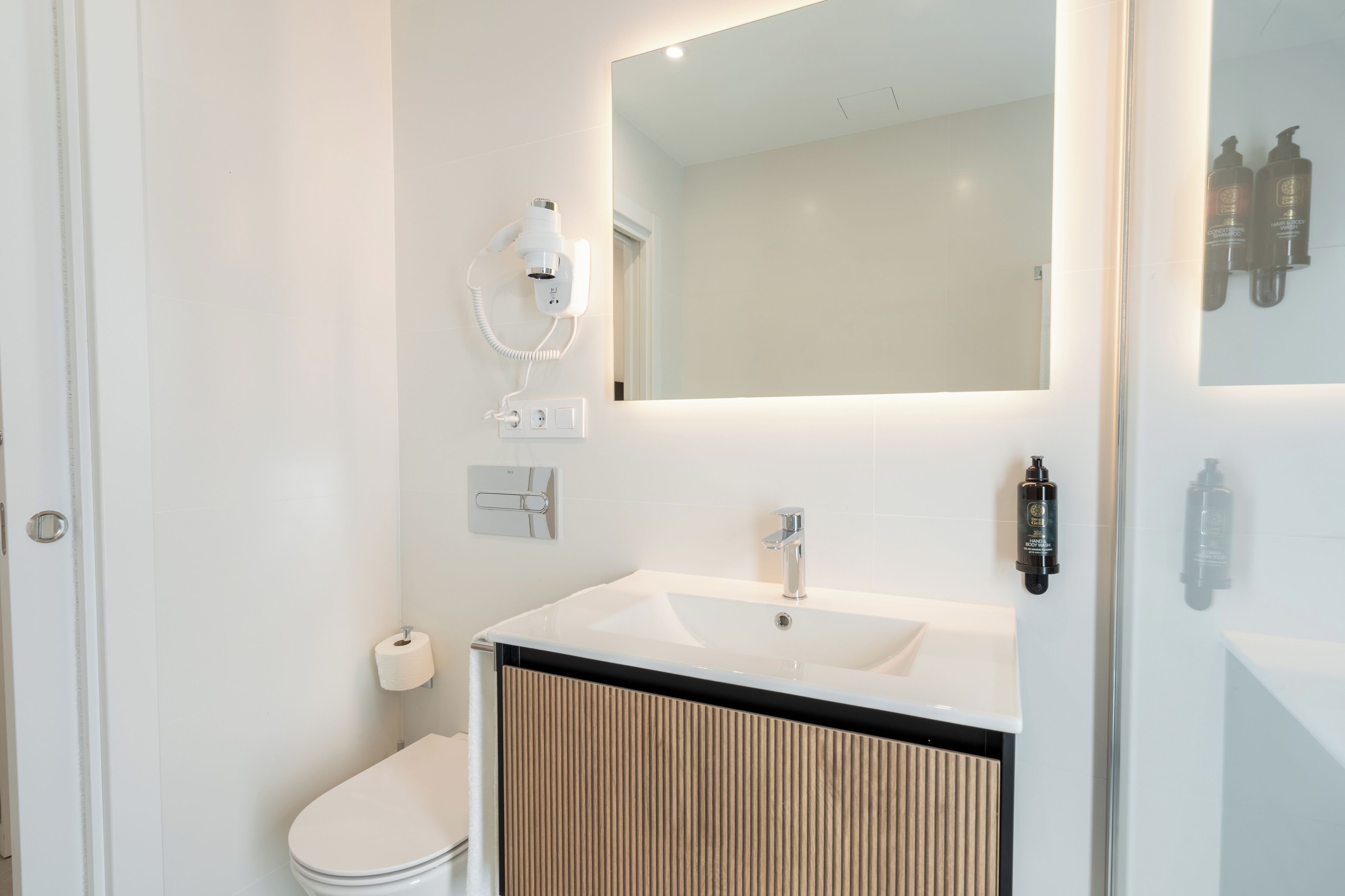 A modern bathroom with a white sink, a mirror, and a hairdryer mounted on the wall.