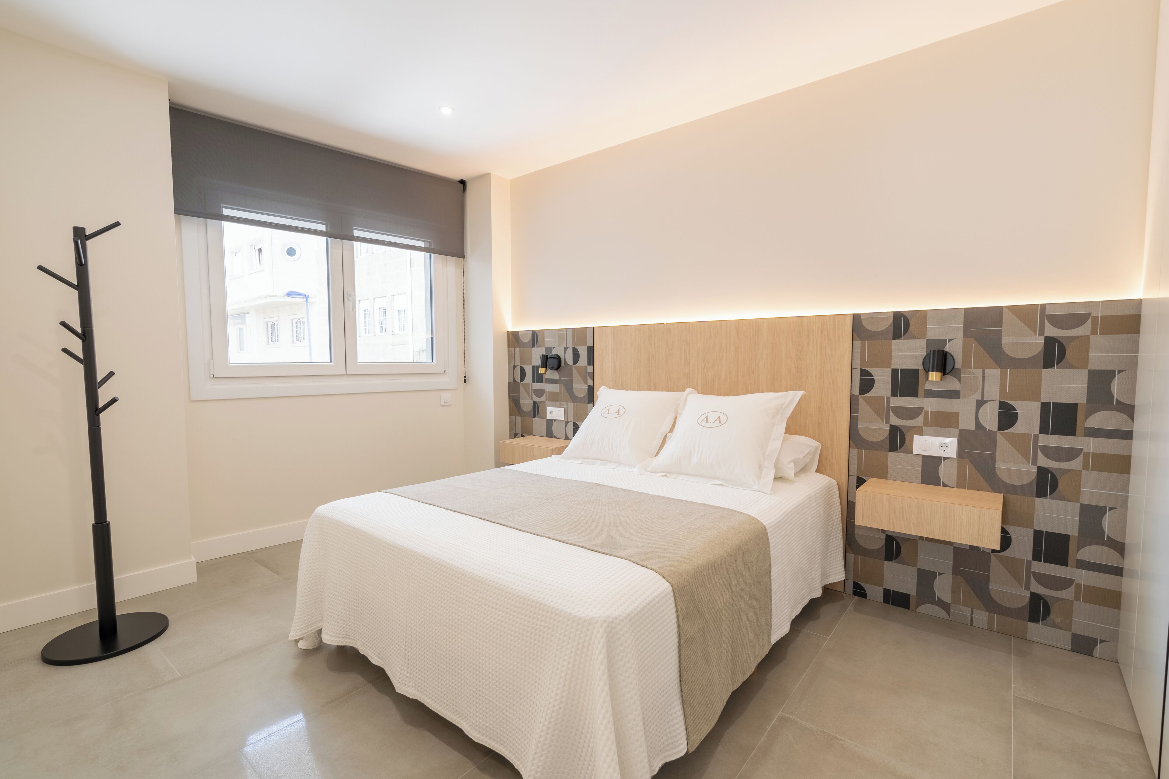 A modern bedroom with a bed, a coat rack, a window, and a wall with a geometric pattern.