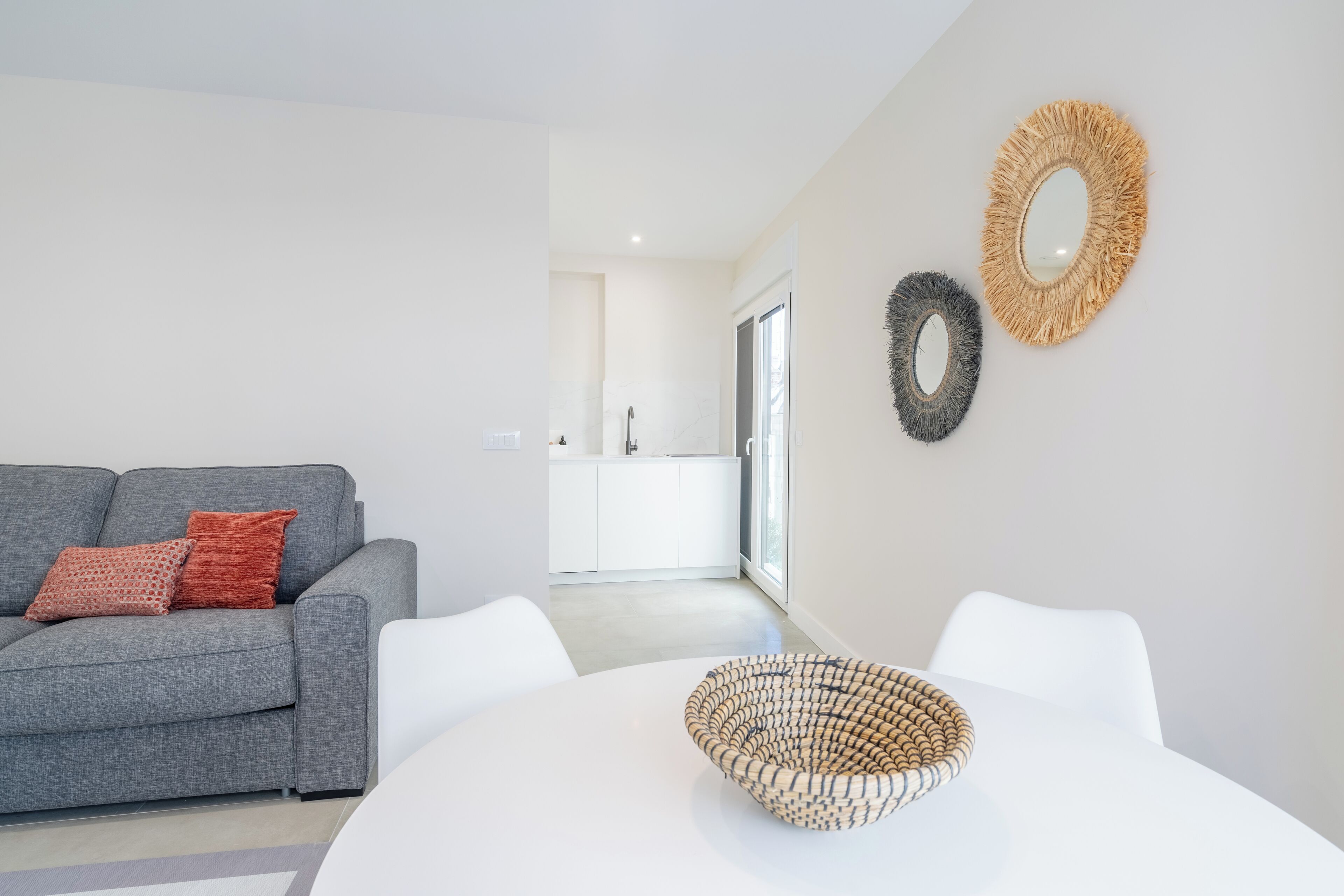 A modern living room with a grey sofa, a white dining table, and a woven basket.