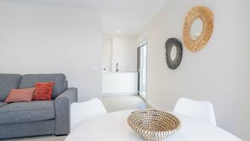 A modern living room with a grey sofa, a white dining table, and a woven basket.