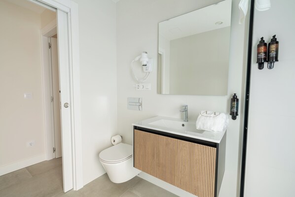 Un baño moderno con inodoro, lavamanos, espejo y secador de pelo.