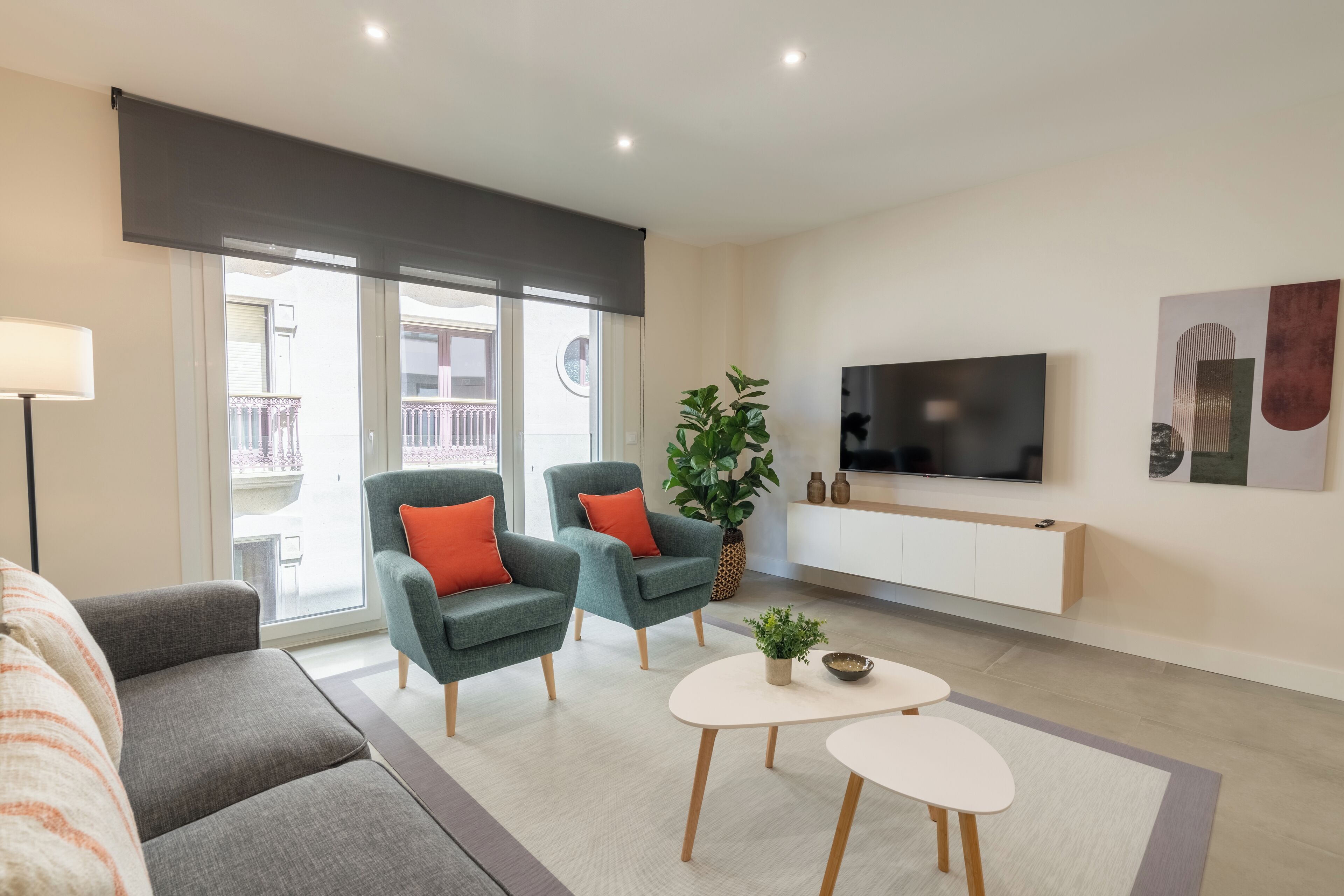 Una sala de estar moderna con un sofá, dos sillones, una mesa de centro, un televisor y un ventanal con vistas al exterior.