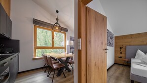 Une cuisine moderne avec un coin repas, un plancher en bois et une grande fenêtre donnant sur la verdure.