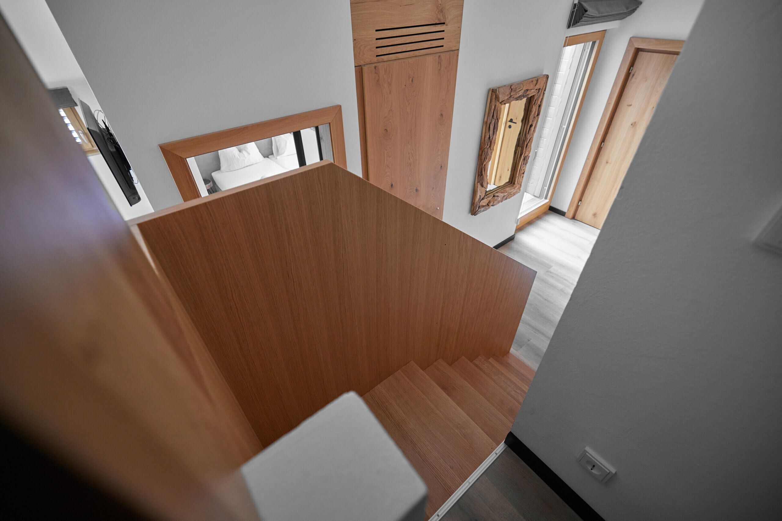 Un intérieur moderne avec un escalier en bois, un mur blanc et un miroir.