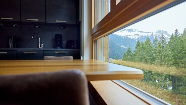 Une cuisine moderne avec des meubles de couleur sombre et une vue sur des montagnes enneigées, visible par une fenêtre.