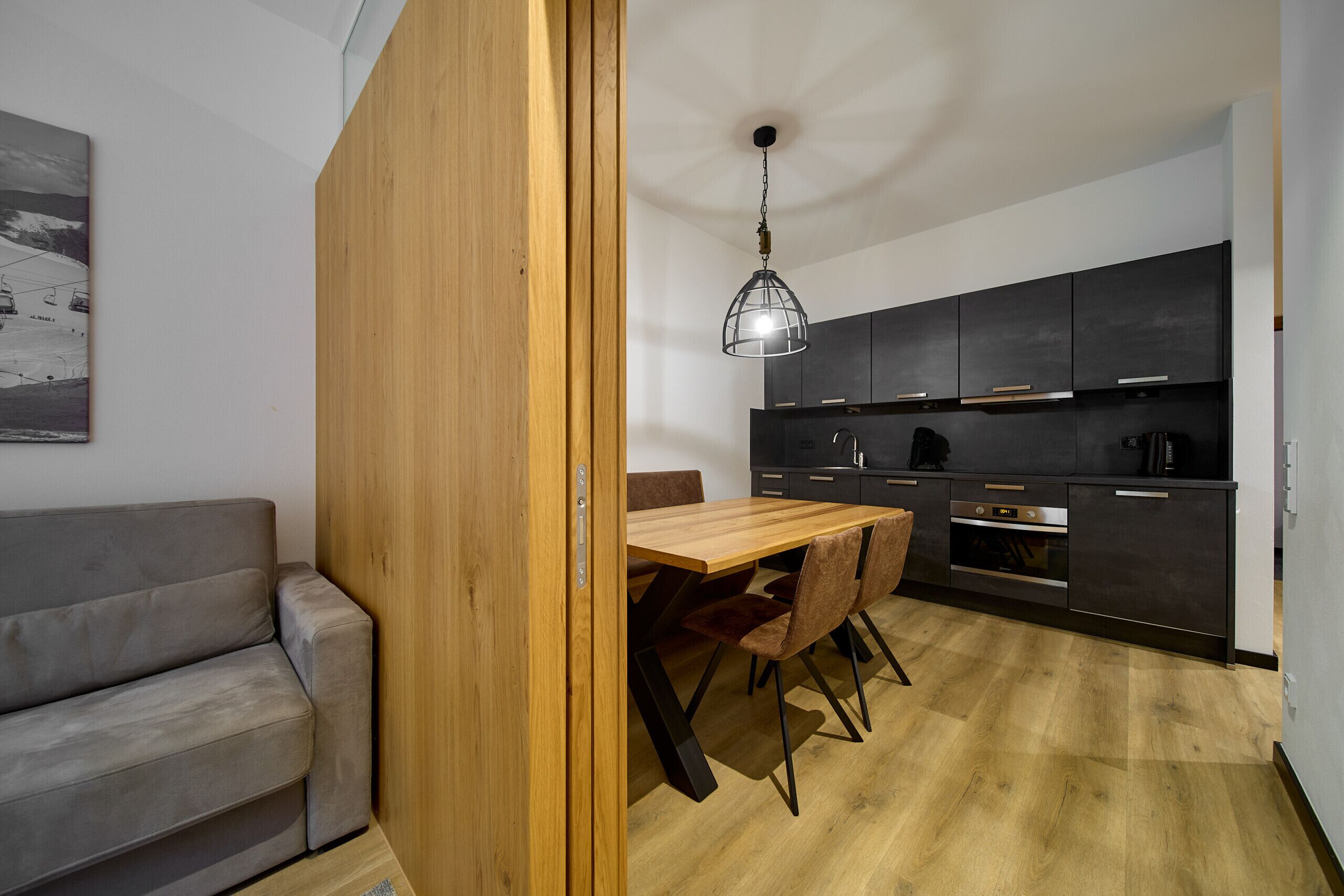 Een moderne keuken met donkere kastjes, een houten eettafel en een hangende lamp.