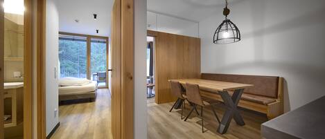A modern interior with a wooden dining table, bench seating, and a large window offering a view of the outdoors.