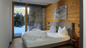 Un dormitorio moderno con una pared de piedra, una cama grande con ropa blanca y un suelo de madera.