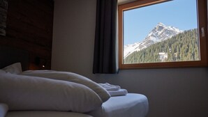 A bedroom with a bed, a window with a mountain view, and a wooden wall.