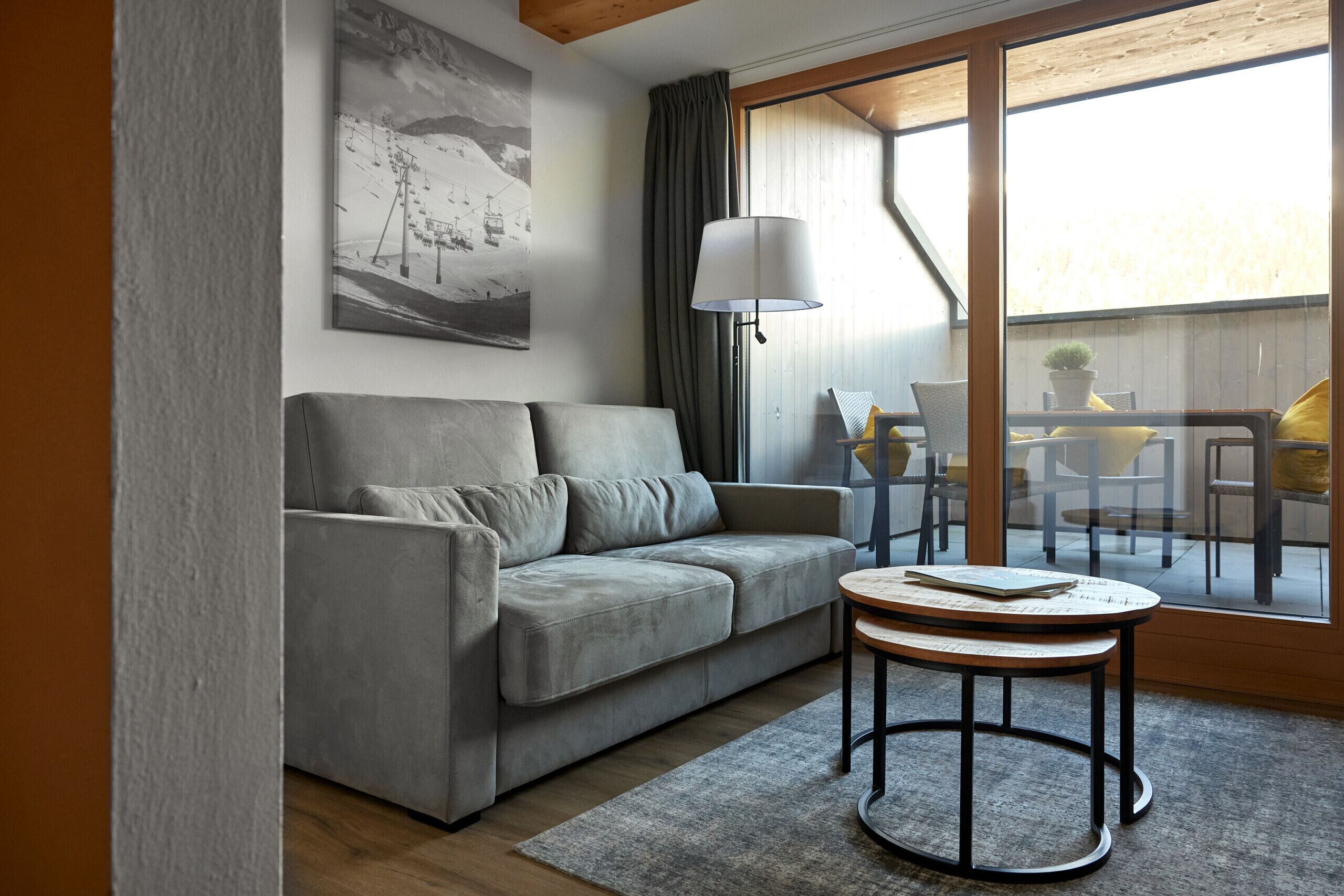 A modern living room with a grey sofa, a round coffee table, and a large window with curtains.