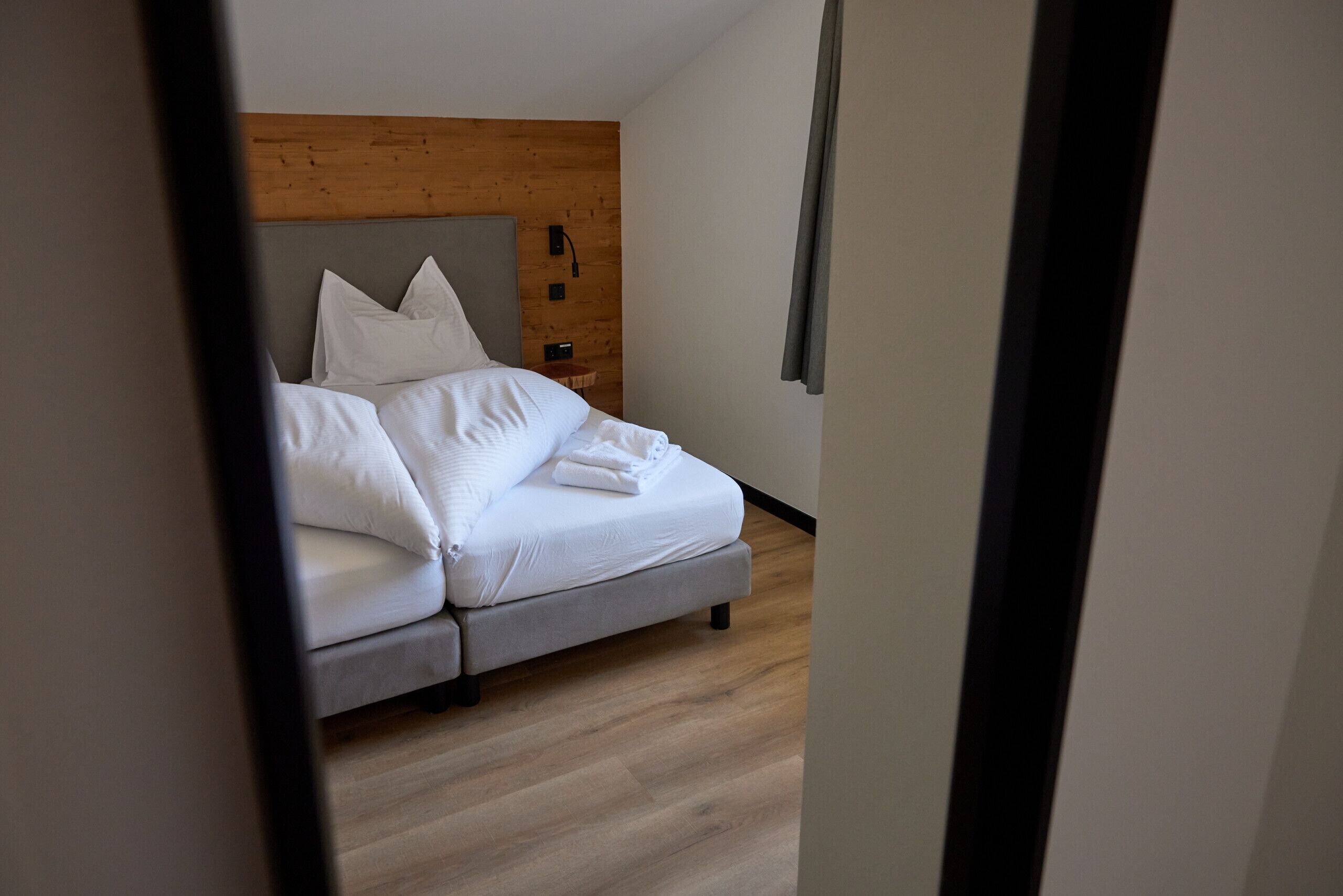 A neatly made bed with white linens in a modern room with wooden paneling and a light-colored floor.
