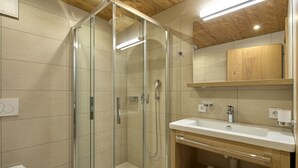 A modern bathroom with a glass-enclosed shower, a white sink, and a wooden vanity.