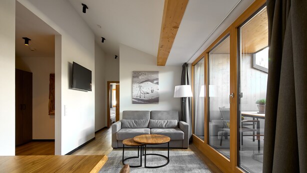 A modern living room with a grey sofa, a round wooden coffee table, and a large window with curtains.