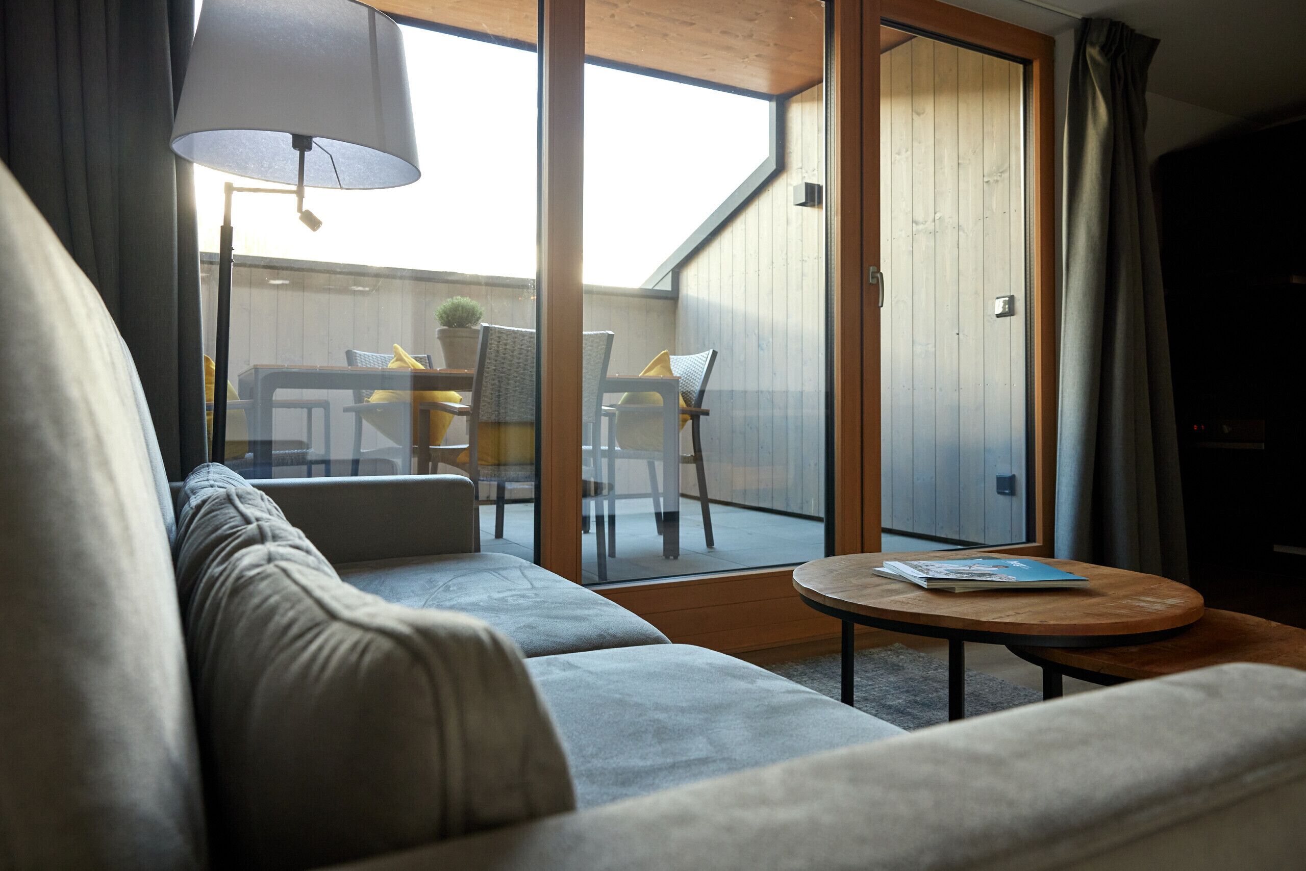 Un salon moderne avec un canapé, une table basse ronde et une vue sur un espace extérieur aménagé en patio, avec une table et des chaises.