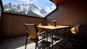 A wooden-paneled room with a table and chairs, a potted plant, and a view of snow-capped mountains through a large window.