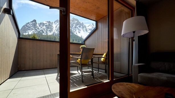 A room with a view of snow-capped mountains, a wooden ceiling, a dining table with chairs, and a lamp.