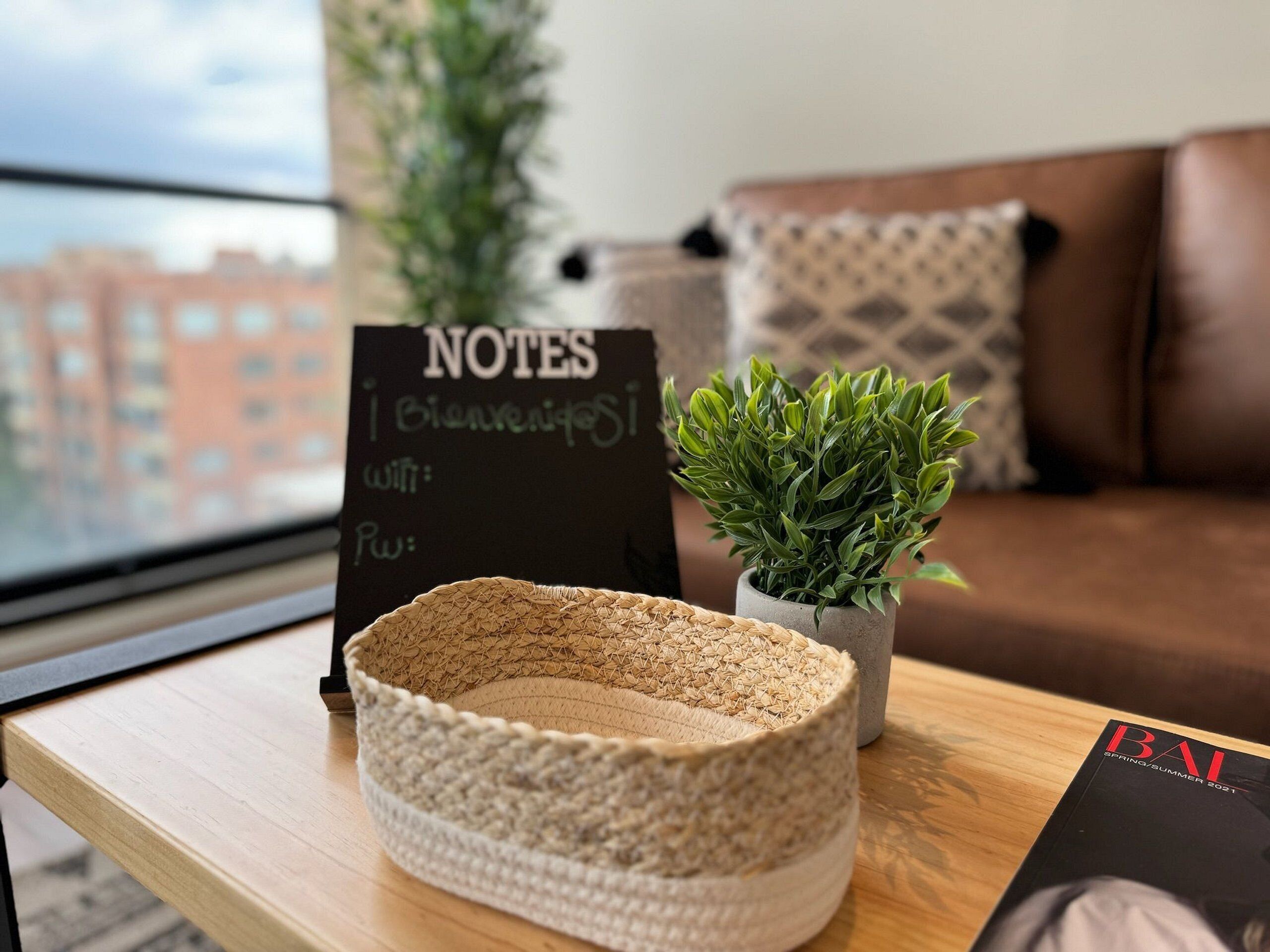 Un salon chaleureux avec un panier tressé posé sur une table en bois, une petite plante en pot et un panneau indiquant « NOTES ».
