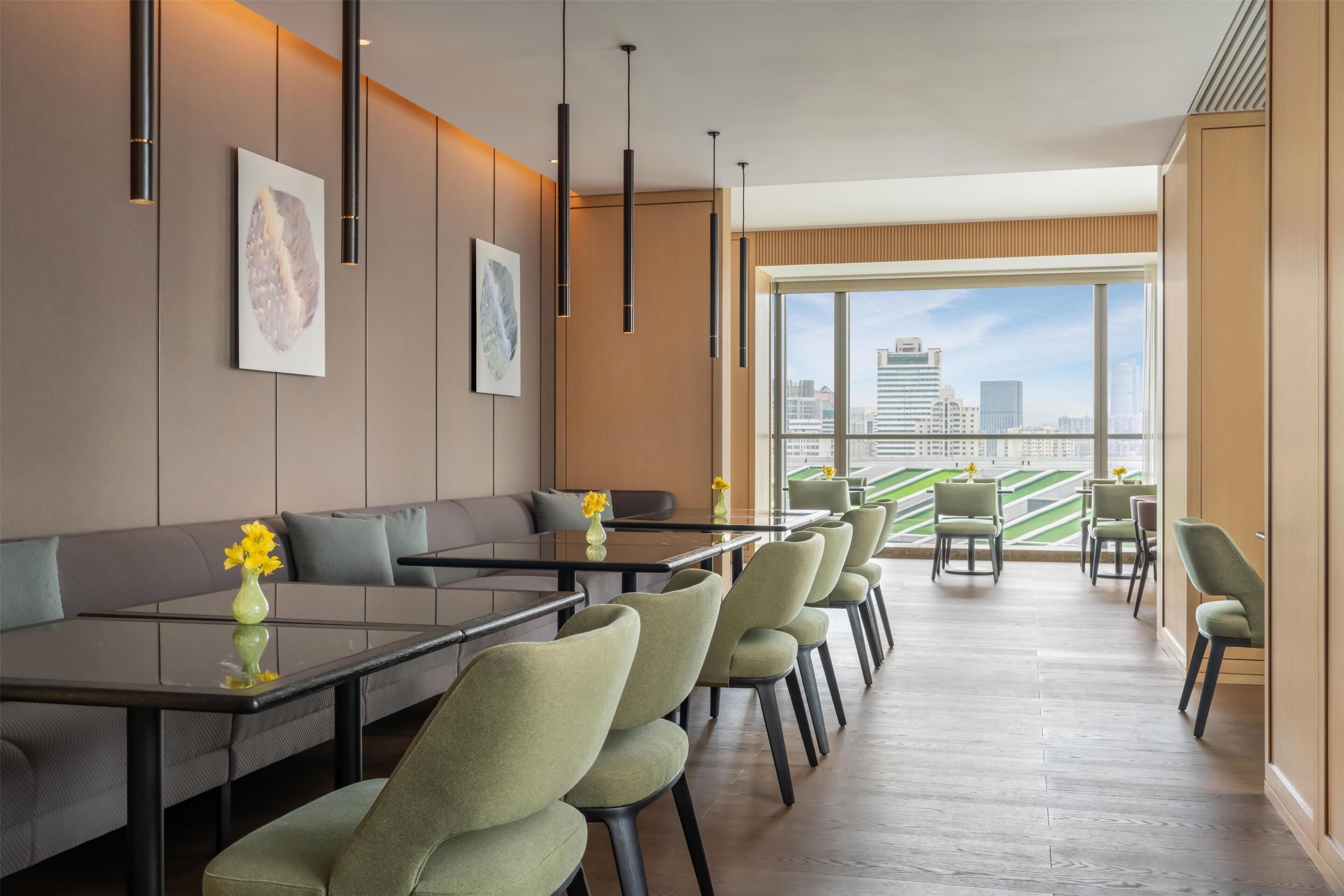 A modern hotel lobby with a long reception desk, seating area, and large windows offering a city view.