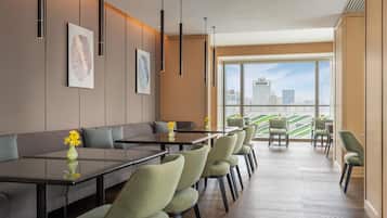 Una hall d'albergo moderna con una lunga reception, un'area salotto e ampie finestre che offrono vista sulla città.