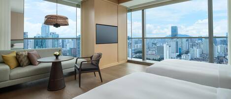 A modern hotel room with a city view, a sofa, a chair, a round table, and a bed.