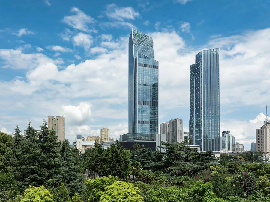 A cityscape with two prominent skyscrapers, surrounded by dense greenery and other buildings.