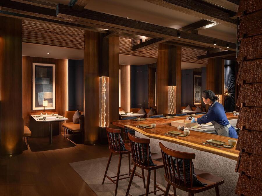 Un restaurante con una barra de madera larga, altos pilares de madera y una persona sirviendo en la barra.
