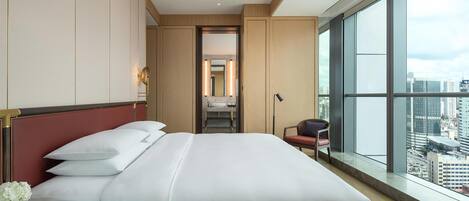 A hotel room with a large bed, a chair, a nightstand, and a view of the city through large windows.