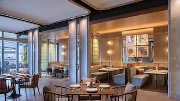 A modern restaurant with indoor seating, large windows, and artwork on the walls.