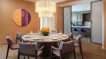 A modern dining area with a round table, chairs, a large pendant light, and a decorative wall piece.
