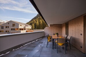 Terraço no telhado com mesa e cadeiras, vista para montanha e floresta, e um edifício ao fundo.