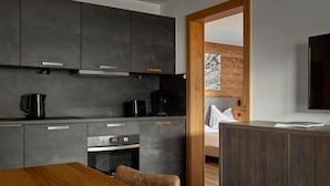 Una cocina moderna con armarios oscuros, una mesa de comedor de madera y vista a una cabaña de madera a través de una puerta abierta.