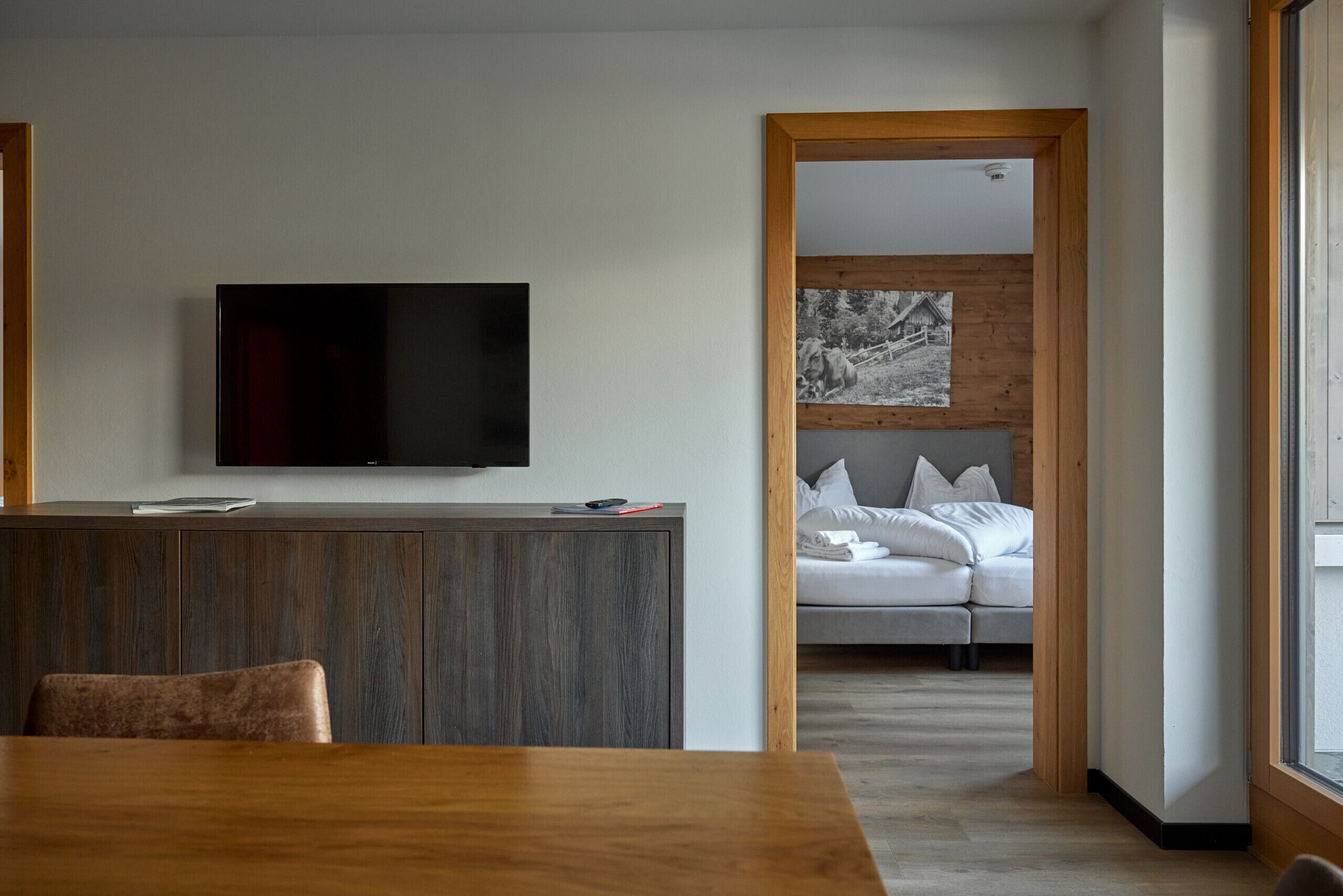 Un soggiorno moderno con un tavolo da pranzo in legno, una TV a schermo piatto montata a parete e un'accogliente zona con divano e cuscini.