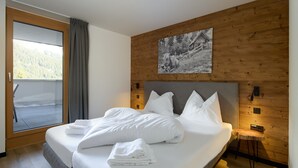 Un lit bien fait, avec du linge de lit blanc et des oreillers, une tête de lit en bois, un petit tabouret en bois et un tableau encadré accroché au mur.