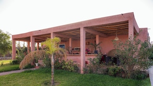 A pink building with a covered patio area, surrounded by greenery and plants. - L'oliviade Village (Marrakech)