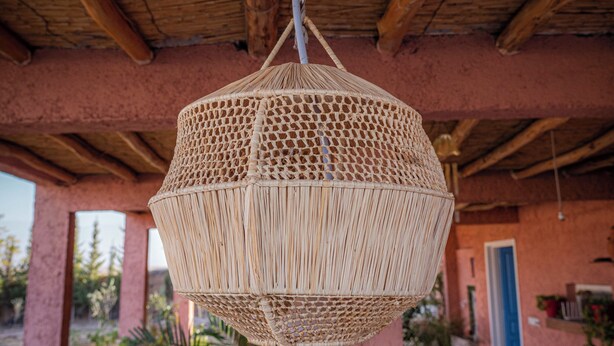 A woven hanging light fixture in a covered outdoor area with wooden beams and a pink wall. - L'oliviade Village (Marrakech)