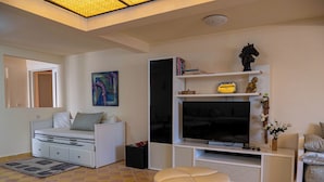 A modern living room with a sofa, ottoman, TV, and artwork. - L'oliviade Village (Marrakech)