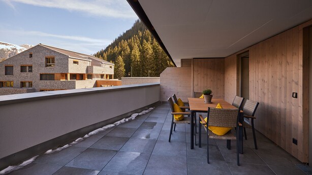 A rooftop terrace with a dining table and chairs, a view of a mountain and forest, and a building in the background. - 59321 Alpen-Krähe 321 (Gargellen)