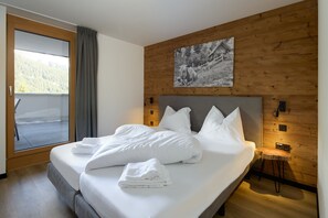 Ein ordentlich bezogenes Bett mit weißen Leinen und Kissen, ein hölzernes Kopfende, ein kleiner Holzschemel und ein gerahmtes Bild an der Wand.