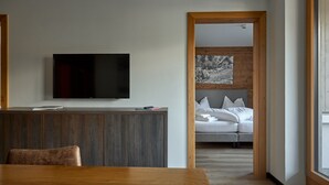 A modern living room with a wooden dining table, a flat-screen TV mounted on the wall, and a cozy seating area with a sofa and pillows. - 59321 Alpen-Krähe 321 (Gargellen)