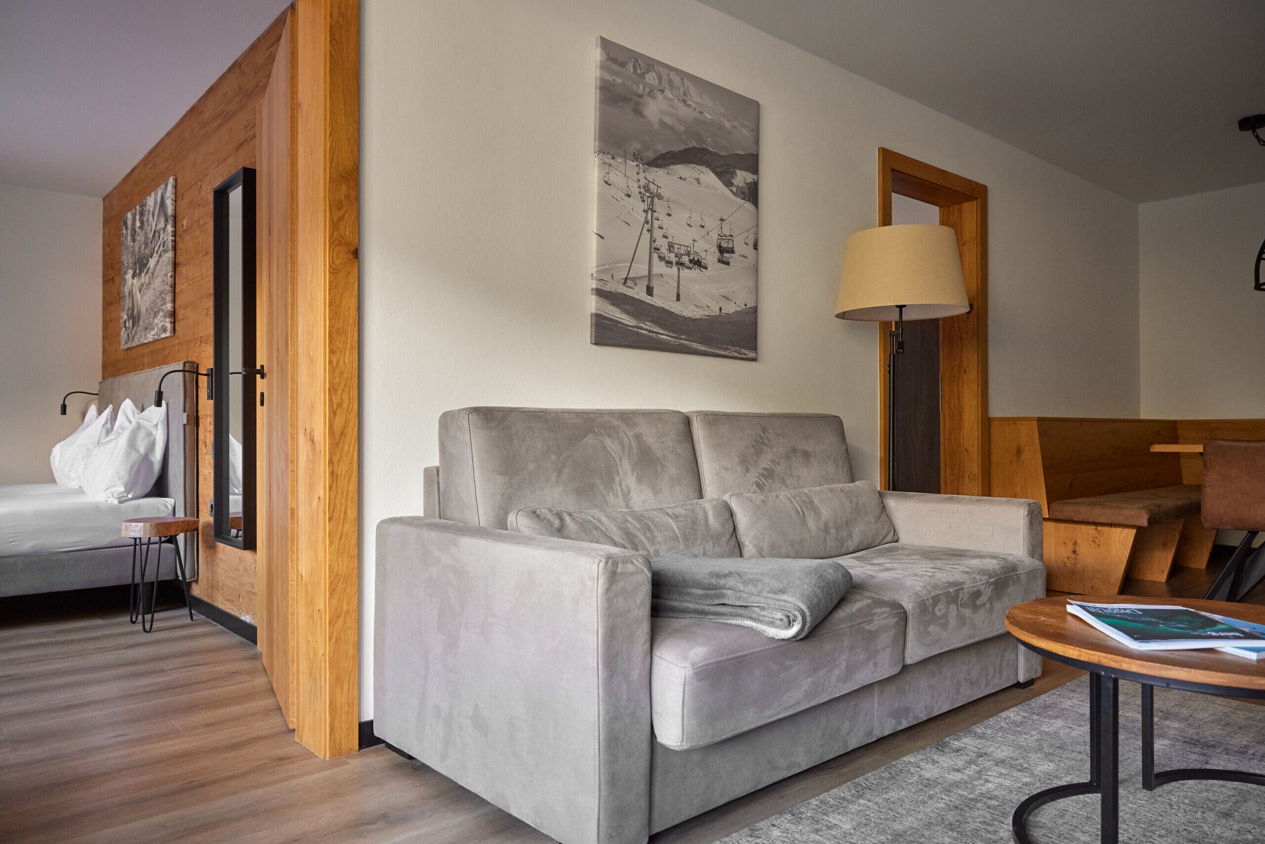 Ein modernes Wohnzimmer mit einem grauen Sofa, einer Holzwand als Akzent und einem Bild mit Ski-Motiv.